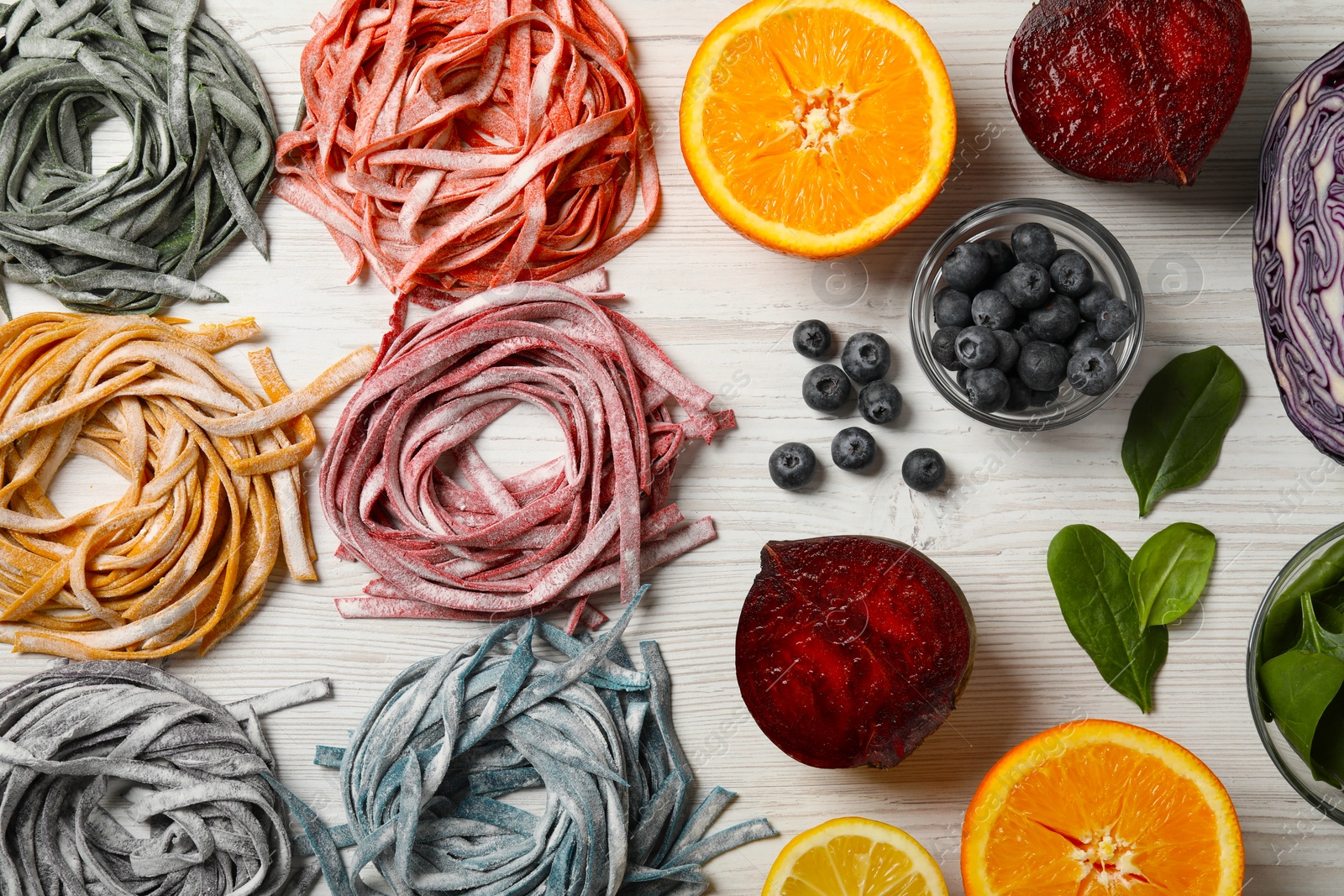 Photo of Rolled pasta painted with natural food colorings and ingredients on white wooden table, flat lay