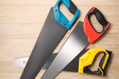 Photo of Saws with colorful handles on wooden background, flat lay