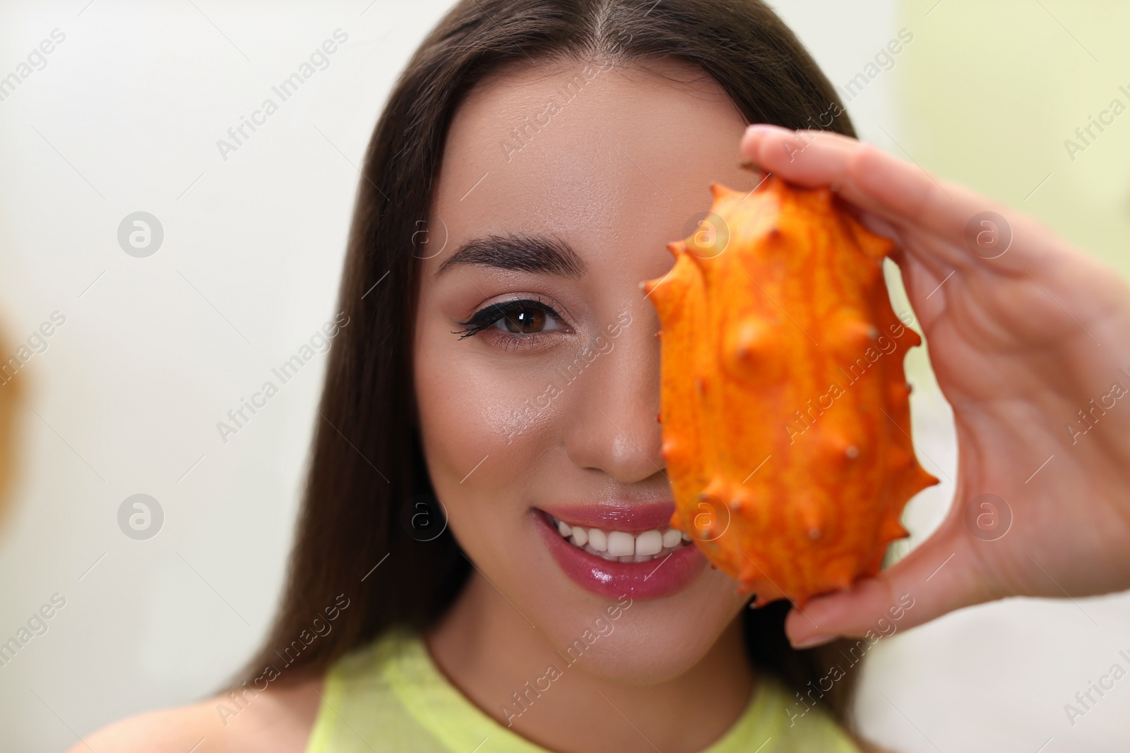 Photo of Young woman with fresh kiwano indoors, closeup. Exotic fruit