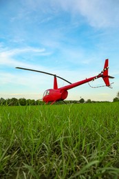 Modern red helicopter on green grass outdoors, low angle view