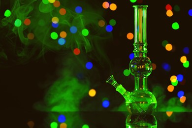 Photo of Glass bong with smoke against blurred lights, space for text. Smoking device