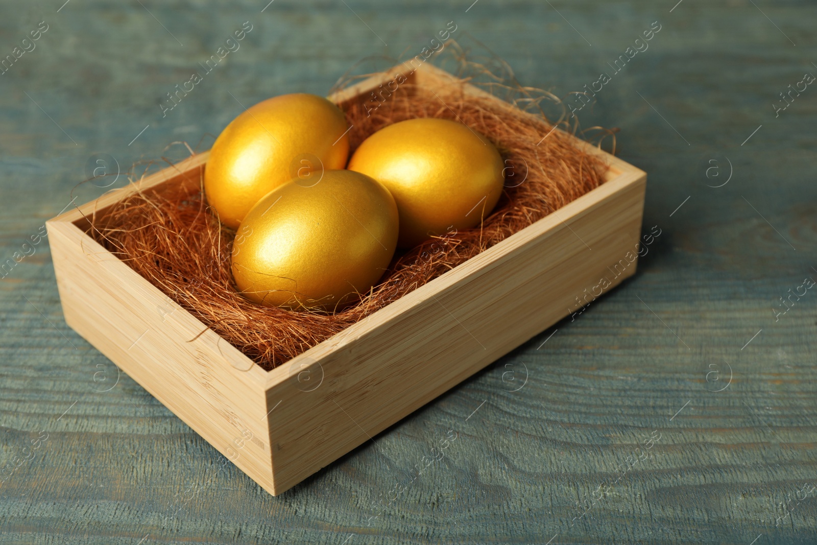 Photo of Crate with golden eggs on light blue wooden table, closeup