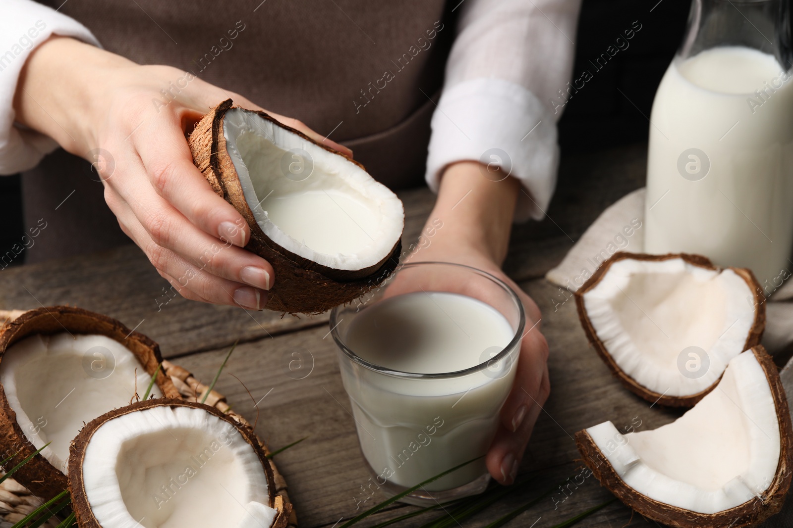 Photo of Woman holding tasty coconut near glass with vegan milk at wooden table, closeup