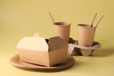 Eco friendly food packaging. Paper containers, cardboard cup holder and straws on pale yellow background