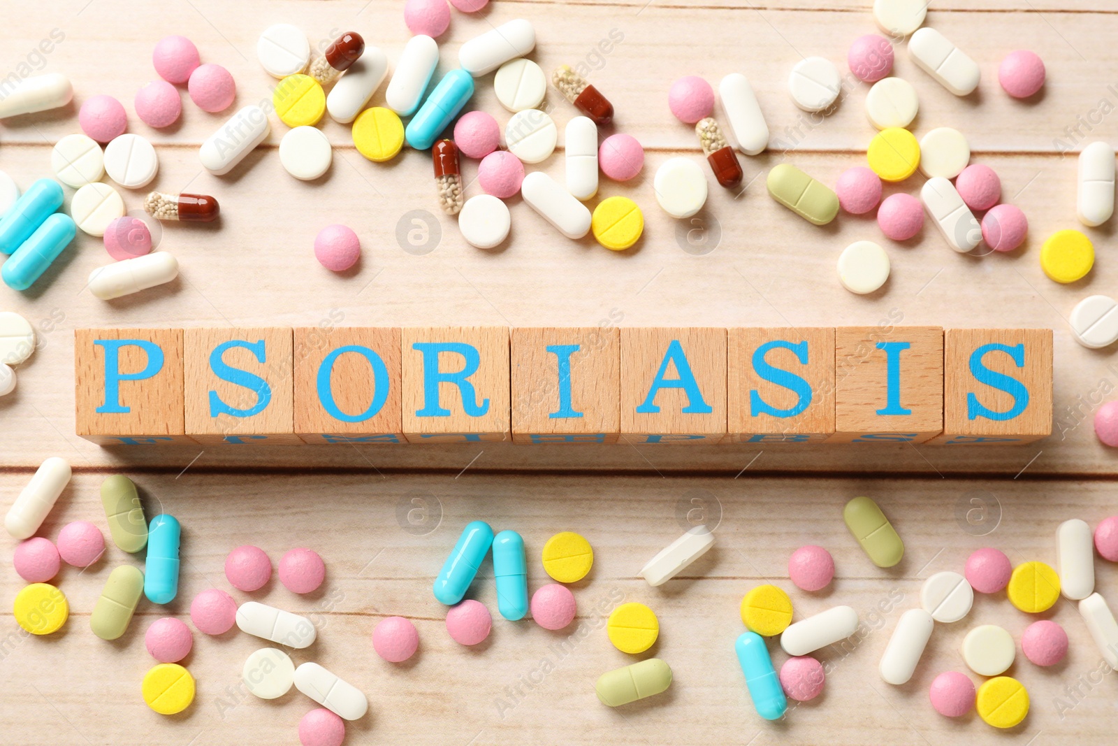 Photo of Word Psoriasis made of cubes with letters and different pills on white wooden table, flat lay