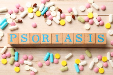 Word Psoriasis made of cubes with letters and different pills on white wooden table, flat lay