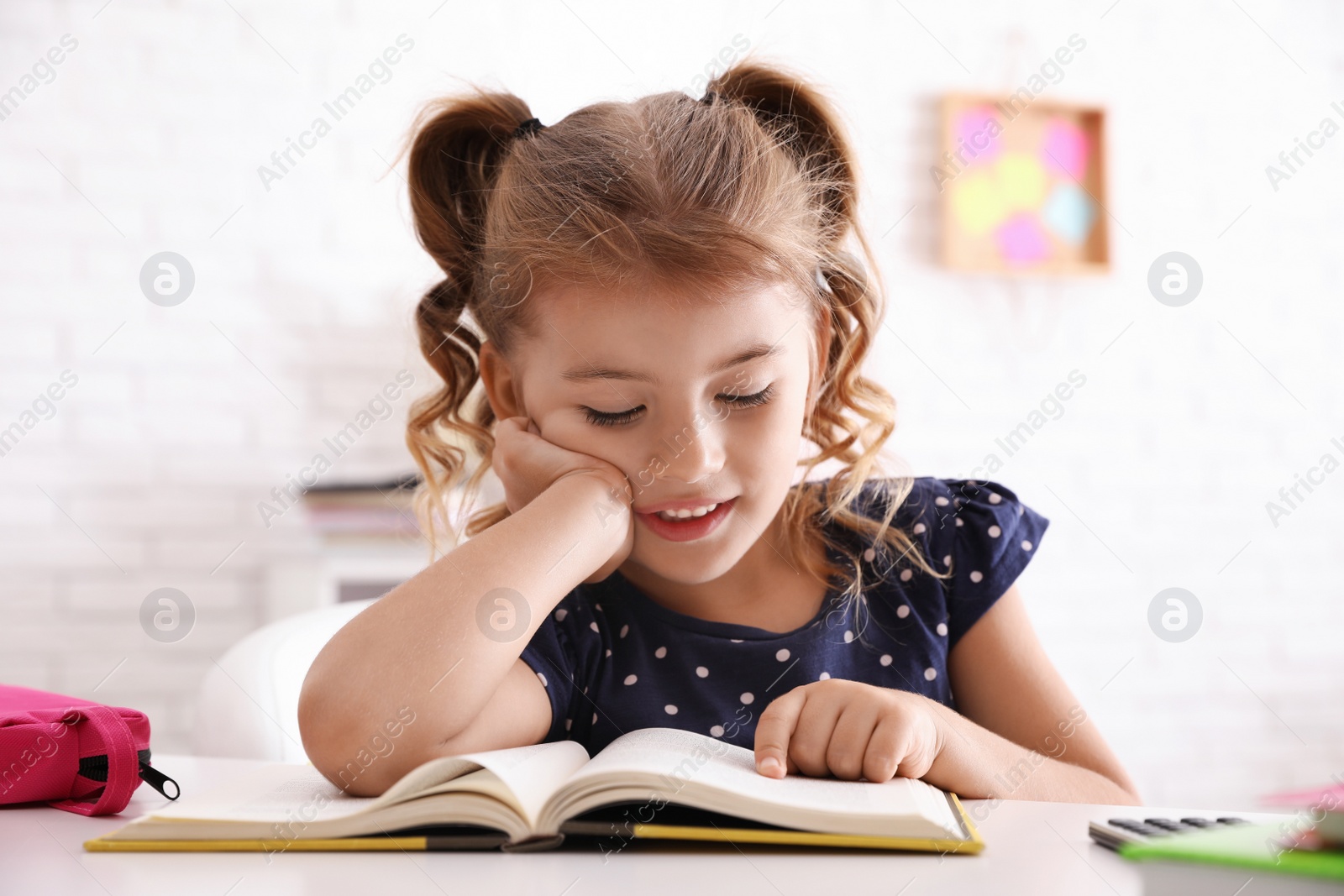 Photo of Cute little girl with book doing homework at table