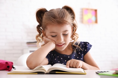 Photo of Cute little girl with book doing homework at table