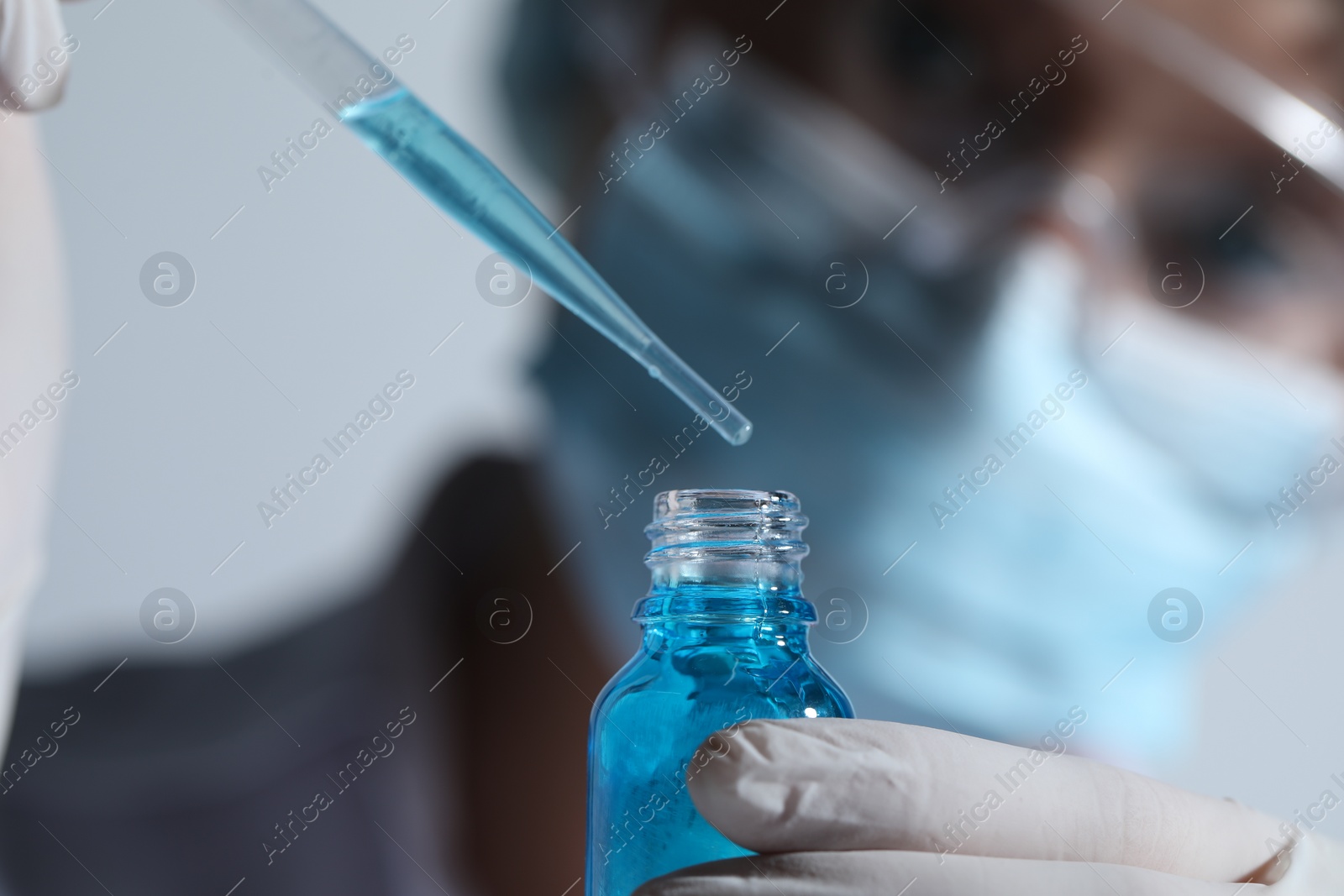 Photo of Scientist dripping liquid from pipette into glass bottle on light background, closeup