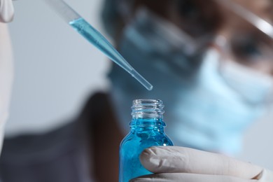 Scientist dripping liquid from pipette into glass bottle on light background, closeup