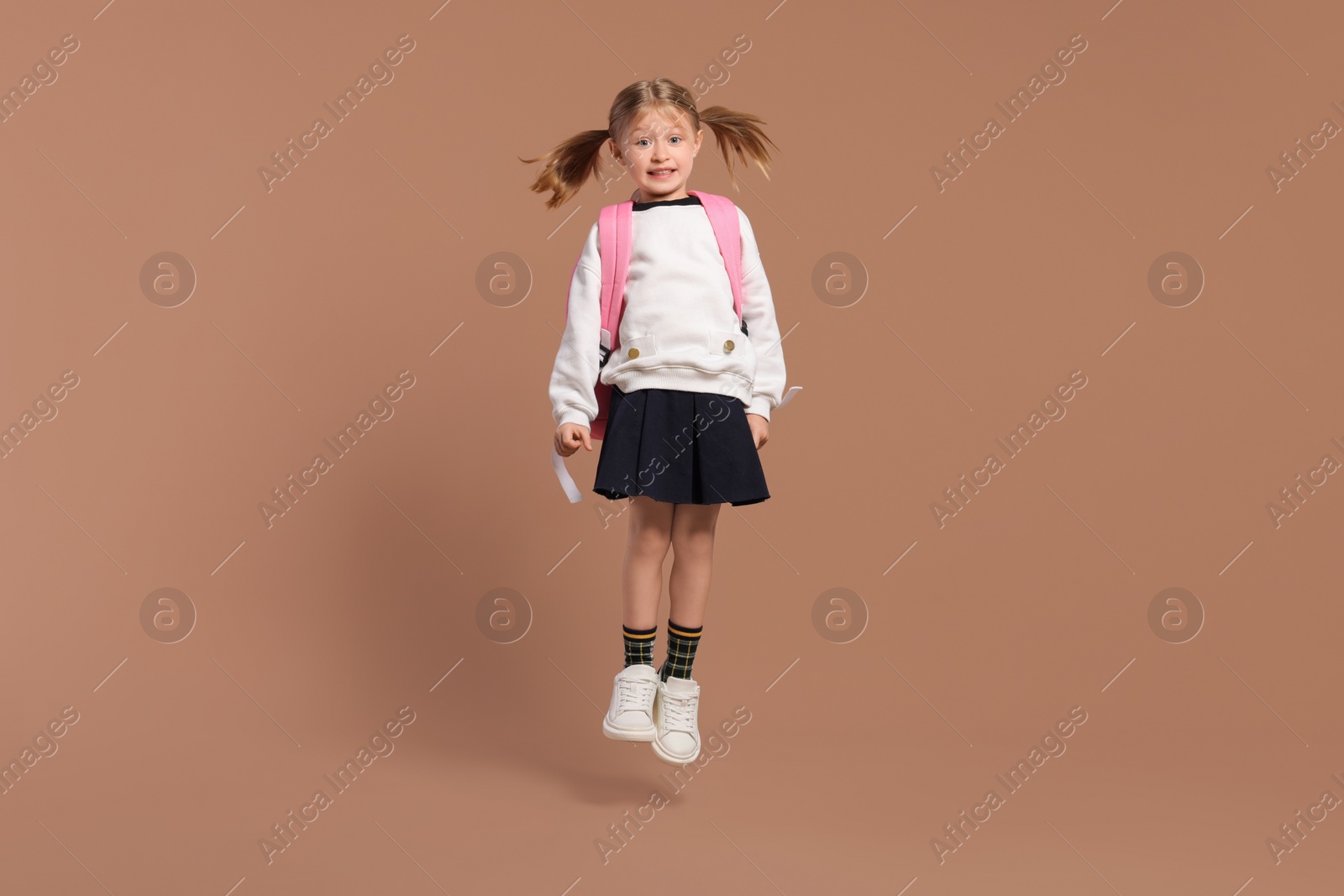 Photo of Happy schoolgirl with backpack jumping on brown background