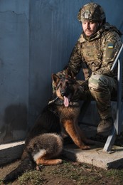 Ukrainian soldier with German shepherd dog sitting outdoors