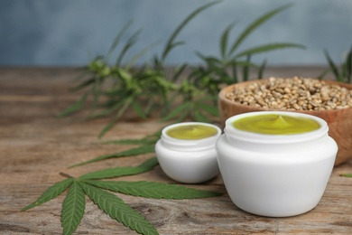 Jars of hemp cream on wooden table against blue background, space for text. Organic cosmetics