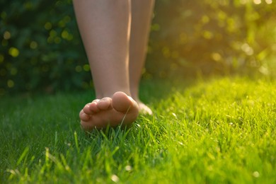 Photo of Teenage girl walking barefoot on green grass outdoors, closeup. Space for text