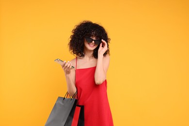 Photo of Happy young woman with shopping bags and modern smartphone on yellow background. Space for text