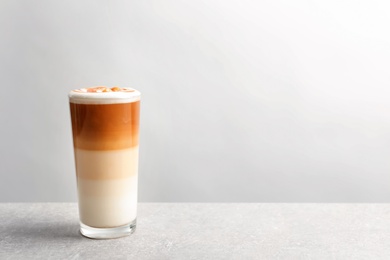 Photo of Glass with delicious caramel latte on table against light background