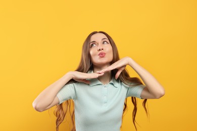 Beautiful young woman blowing kiss on yellow background
