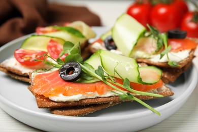 Photo of Tasty rye crispbreads with salmon, cream cheese and cucumber on plate, closeup
