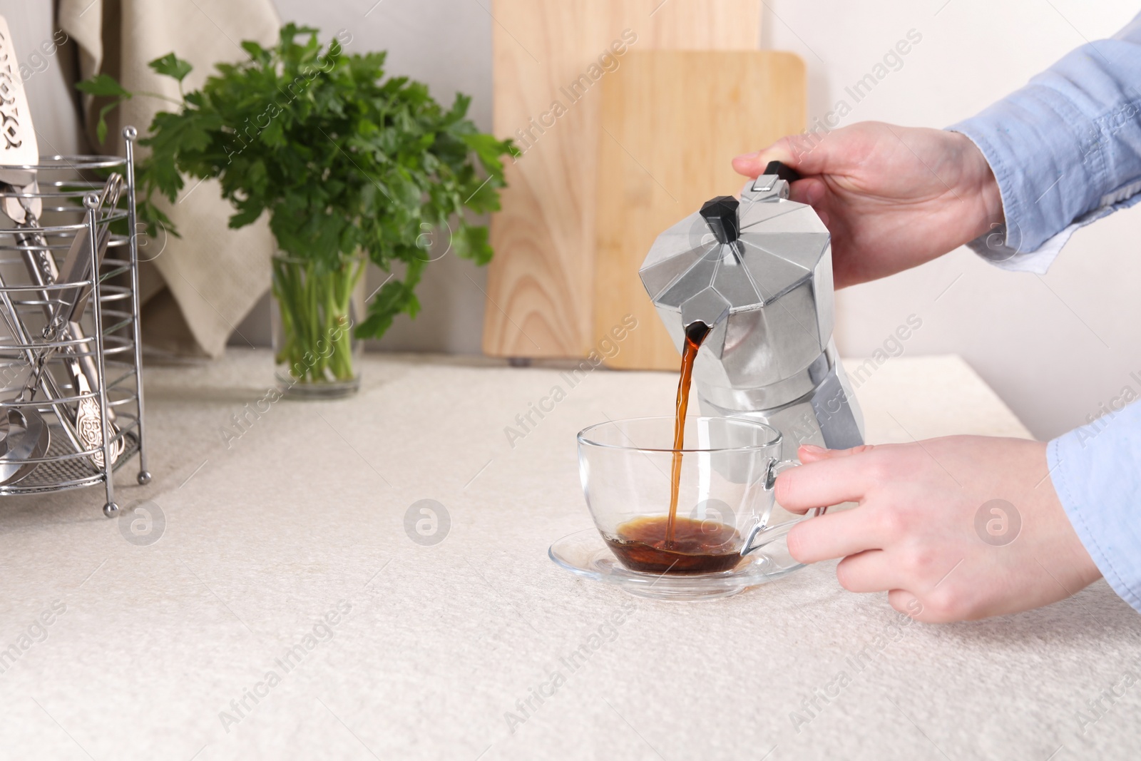 Photo of Woman pouring aromatic coffee from moka pot into glass cup at light textured table, closeup. Space for text