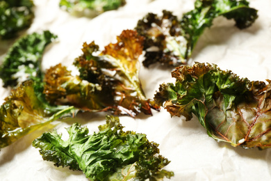 Tasty baked kale chips on parchment paper, closeup