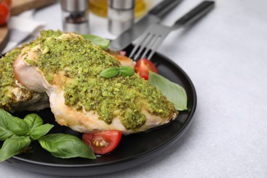 Delicious chicken breasts with pesto sauce, tomatoes and cutlery served on light table, closeup