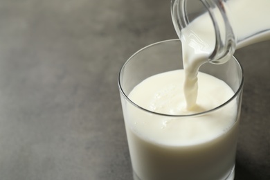 Photo of Pouring milk into glass on grey table, closeup. Space for text