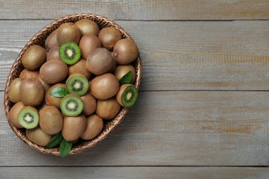 Photo of Fresh ripe kiwis in wicker bowl on wooden table, top view. Space for text