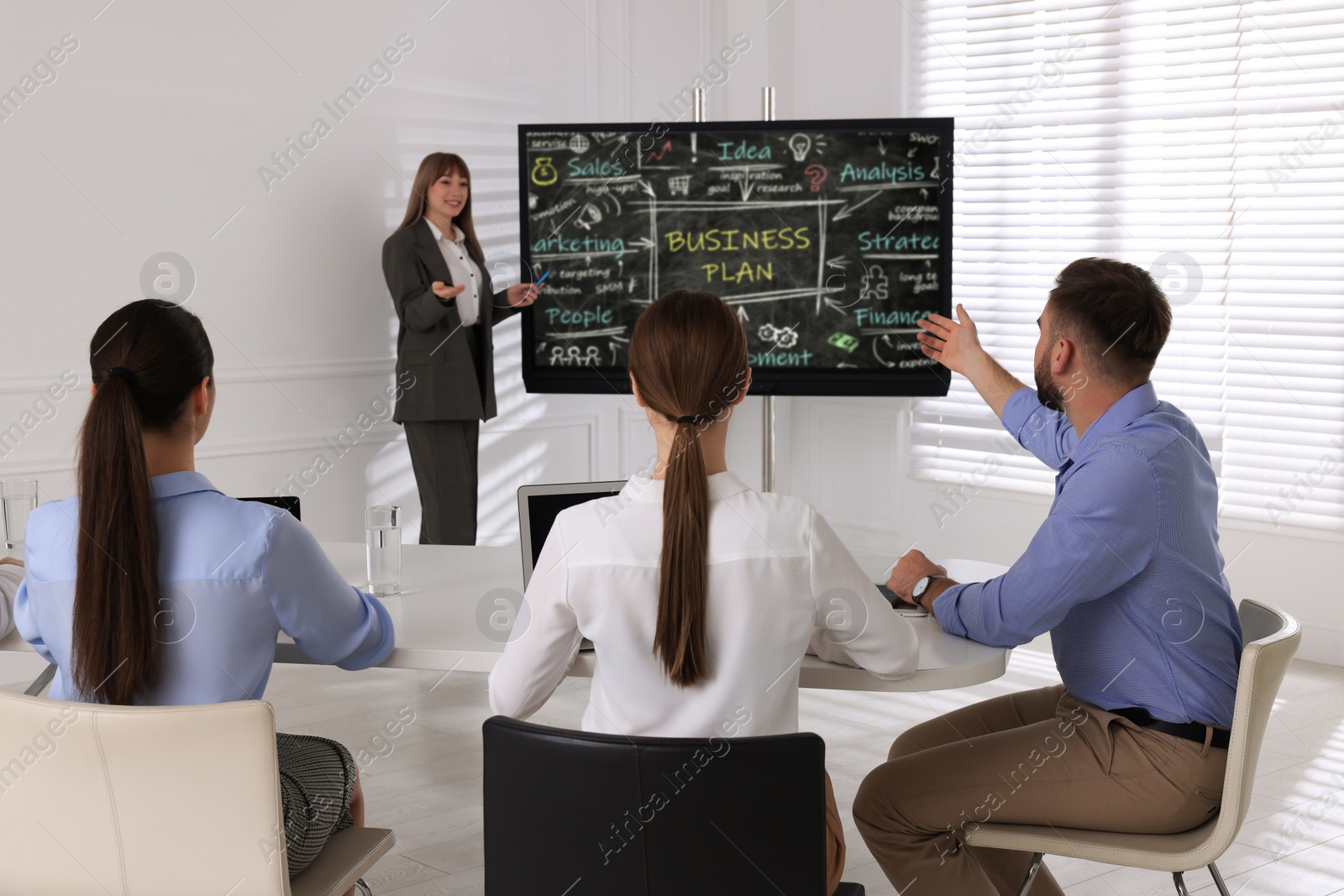 Photo of Business trainer near interactive board in meeting room during presentation, focus on colleagues