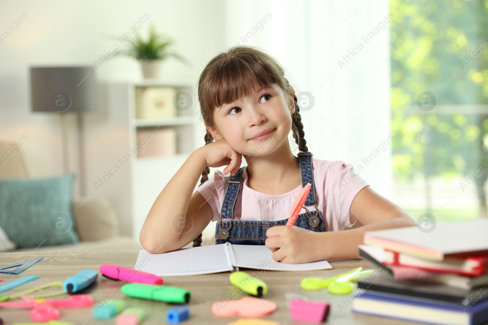 Photo of Cute girl doing homework at table with school stationery indoors