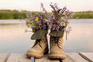 Photo of Boots with beautiful wild flowers on wooden pier near lake
