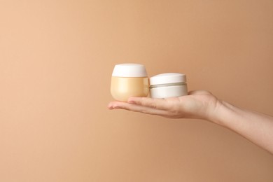 Photo of Woman holding jars of face cream on beige background, closeup. Space for text