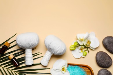 Flat lay composition with herbal massage bags and other spa products on beige background, space for text