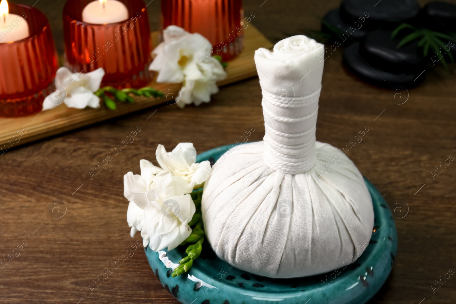 Photo of Herbal massage bag, burning candles and spa stones on wooden table