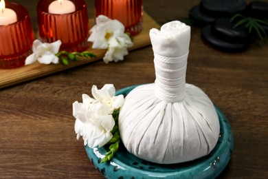 Photo of Herbal massage bag, burning candles and spa stones on wooden table