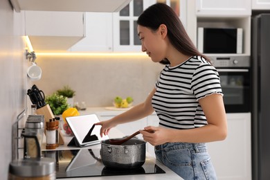 Photo of Woman looking at recipe on tablet while cooking in kitchen