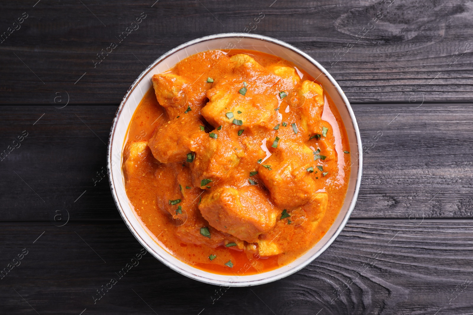 Photo of Bowl of delicious chicken curry on black wooden table, top view