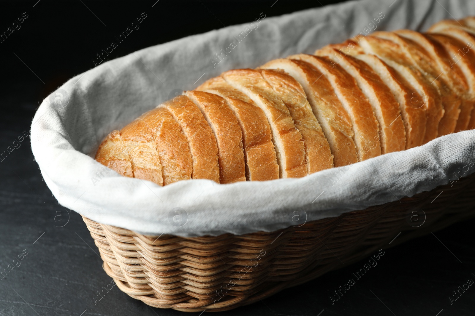 Photo of Slices of bread in basket on black table, closeup