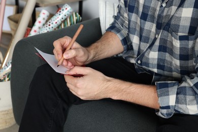 Photo of Man writing message in greeting card on sofa in room, closeup