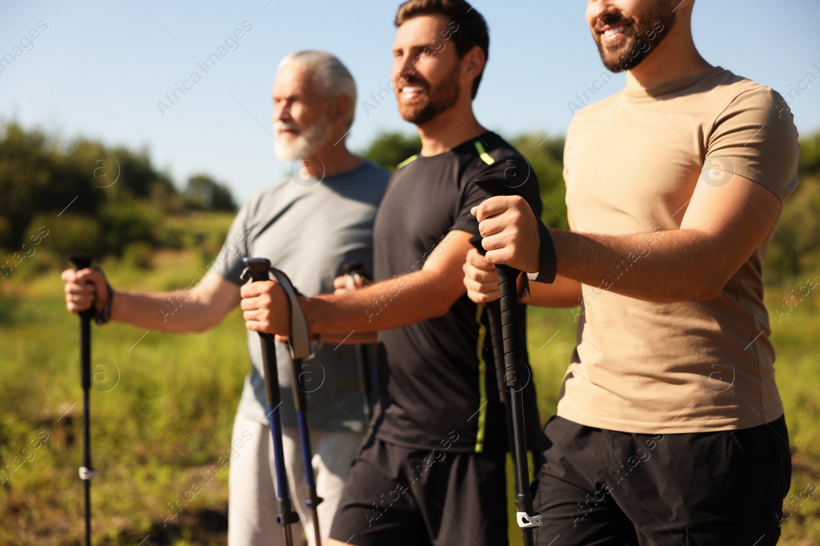 Photo of Happy men practicing Nordic walking with poles outdoors on sunny day, selective focus