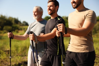 Happy men practicing Nordic walking with poles outdoors on sunny day, selective focus