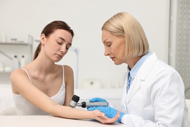 Photo of Dermatologist with dermatoscope examining patient at white table in clinic