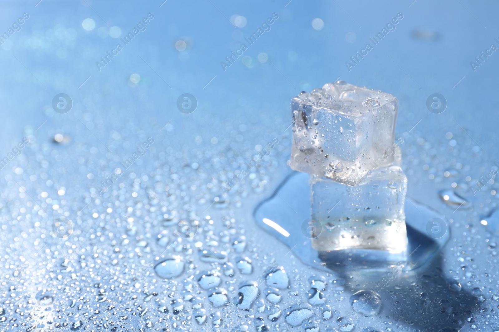 Photo of Melting ice cubes and water drops on light blue background, closeup. Space for text