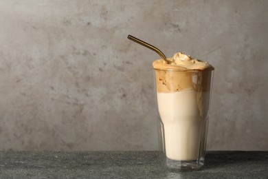 Photo of Glass of delicious dalgona coffee on grey textured table, space for text