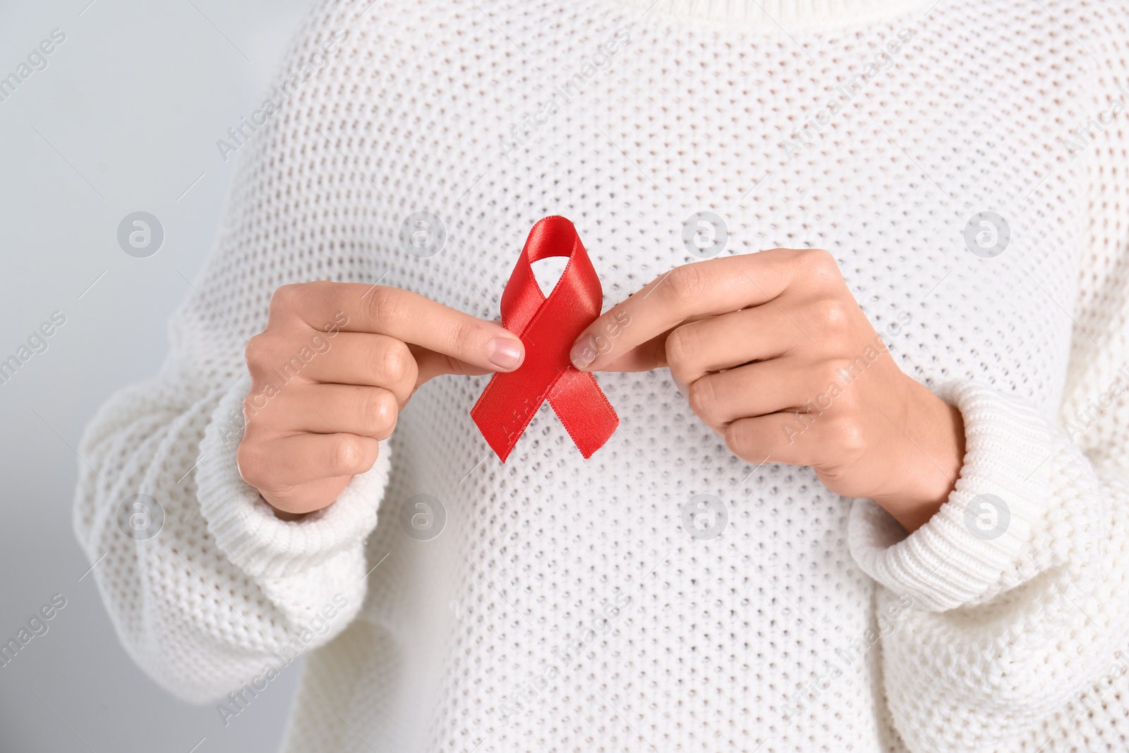 Photo of Woman holding red awareness ribbon on light background, closeup. World AIDS disease day