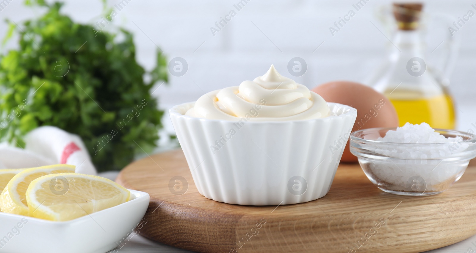 Photo of Fresh mayonnaise sauce in bowl and ingredients on table