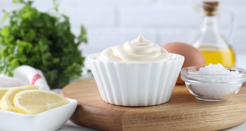 Photo of Fresh mayonnaise sauce in bowl and ingredients on table