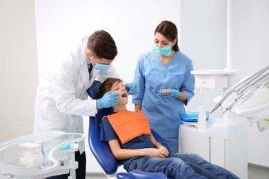 Photo of Professional dentist and assistant working with little boy in clinic