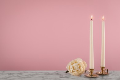 Photo of Elegant candlesticks with burning candles and flower on white marble table. Space for text