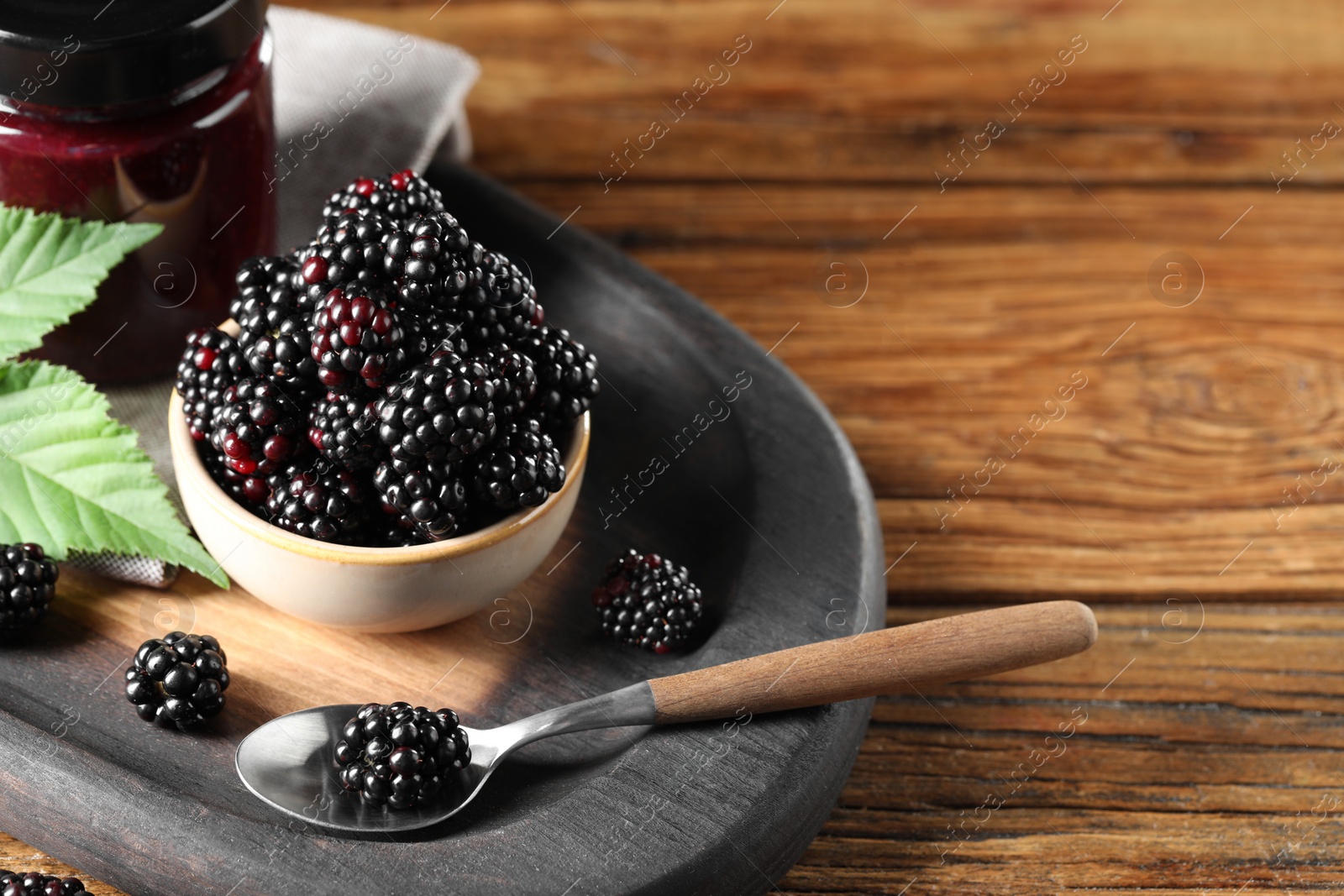 Photo of Fresh ripe blackberries, tasty jam and leaves on wooden table. Space for text