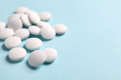 Photo of Many white pills on light blue background, closeup. Space for text